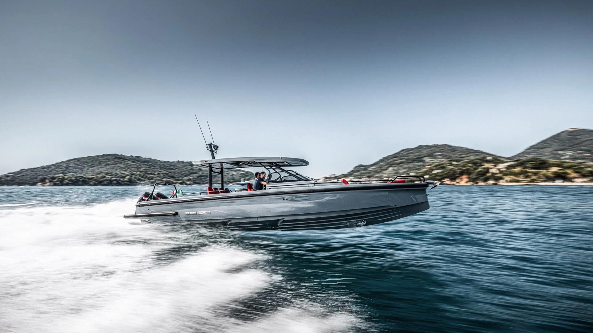Bateau Bravis Marine gris ancré en eau turquoise près d'une plage méditerranéenne avec collines boisées en arrière-plan