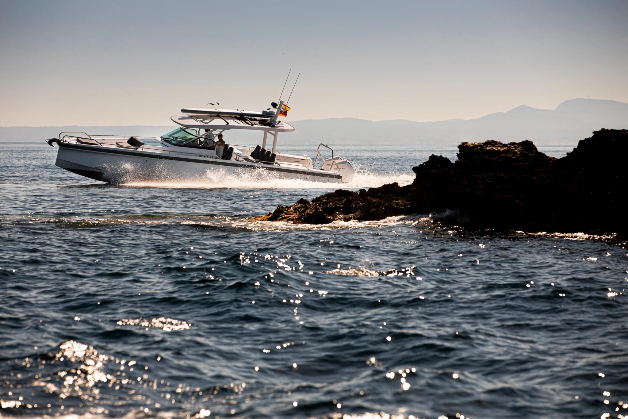 Bateau Axopar naviguant près des rochers en mer avec montagnes en arrière-plan