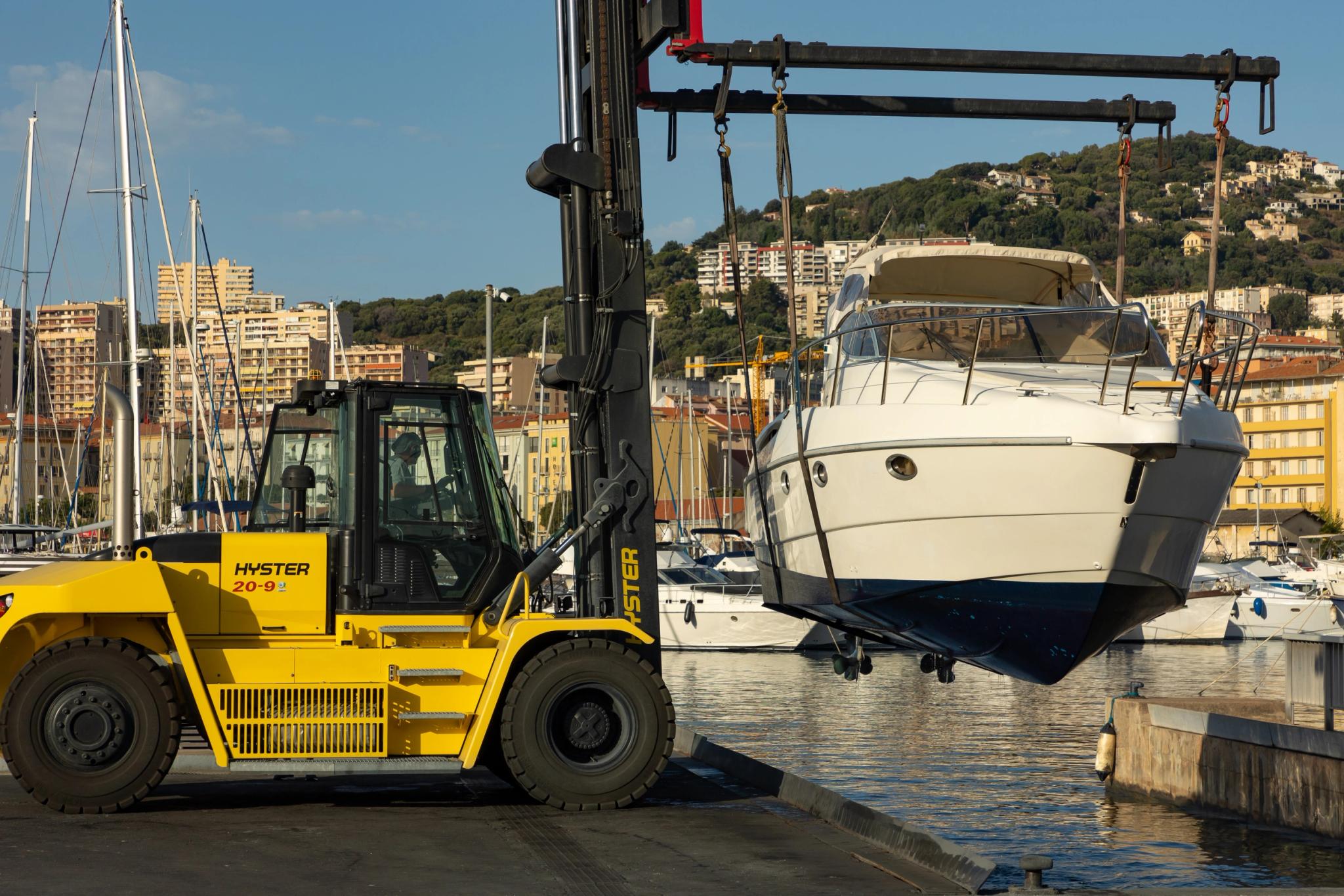 Chantier naval avec chariot élévateur Hyster soulevant un bateau blanc en Méditerranée