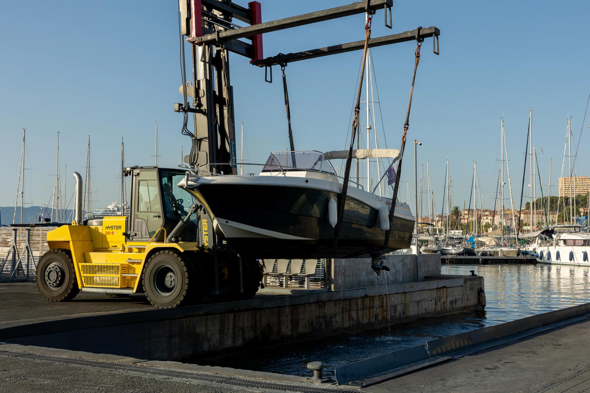 Chariot élévateur jaune soulevant un bateau au chantier naval avec grue portuaire