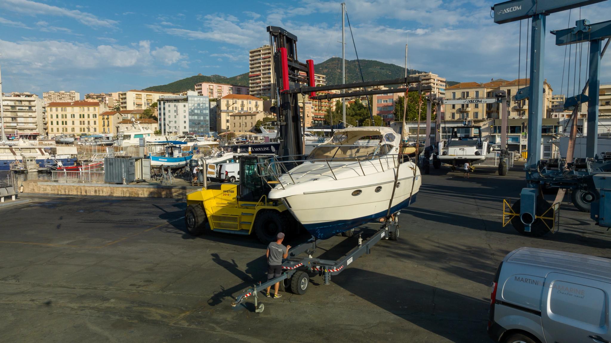 Chantier naval avec chariot élévateur déplaçant un bateau blanc à moteur
