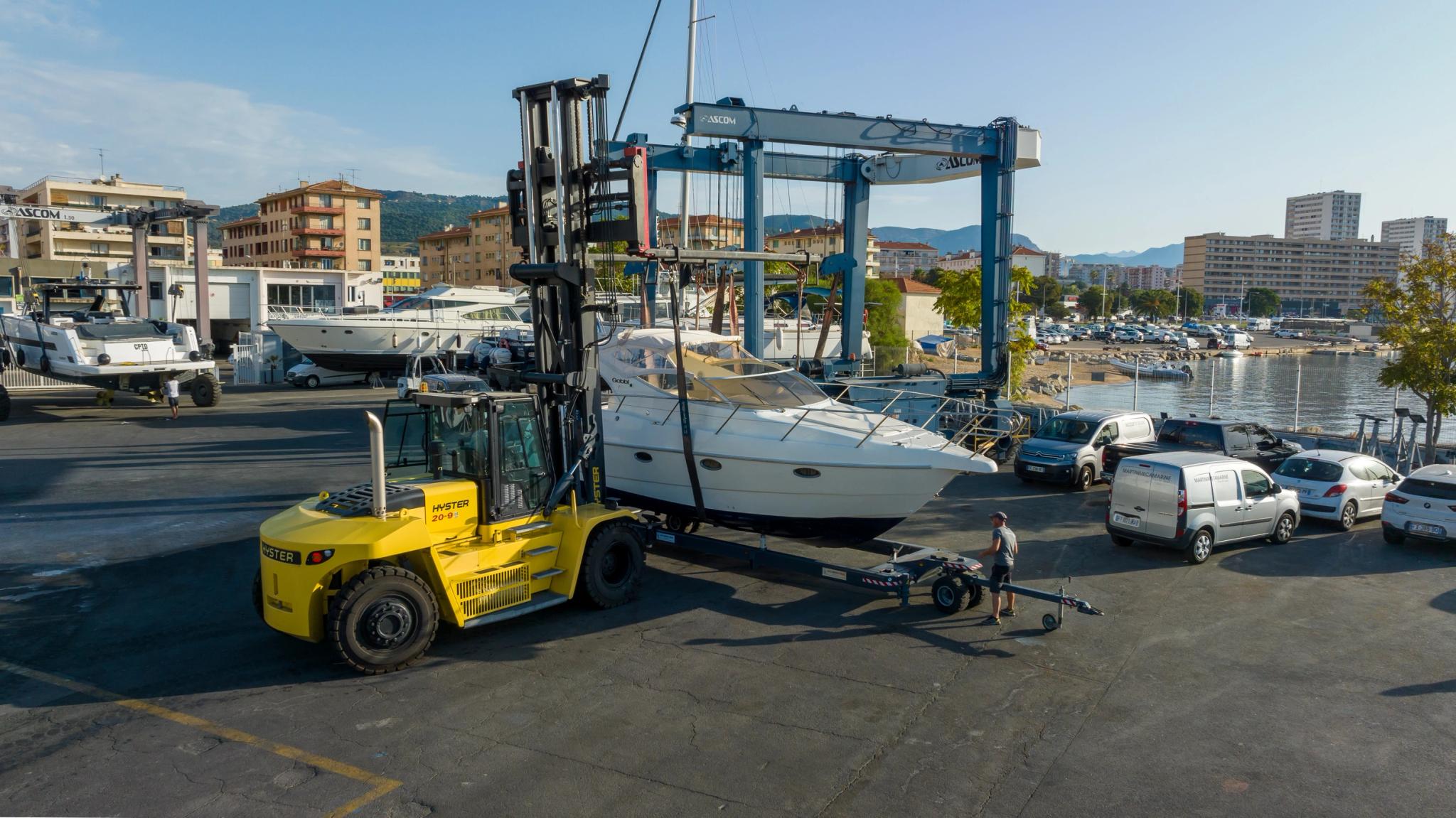 Chantier naval avec chariot élévateur jaune manipulant un bateau de plaisance sous portique