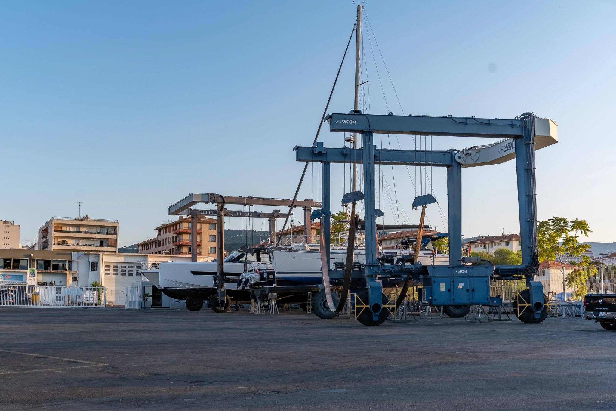 Chantier naval avec grue portuaire levant un voilier blanc en réparation